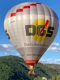 Hei&szlig;luftballon beim Start vor bewaldeten H&uuml;gel.